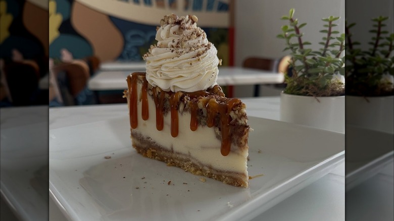 Close-up of cheesecake slice dripping with caramel and topped with whipped cream on white platter