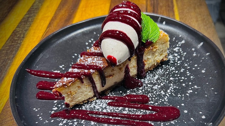 Cheesecake slice topped with berry compote, mint leaf, ice cream