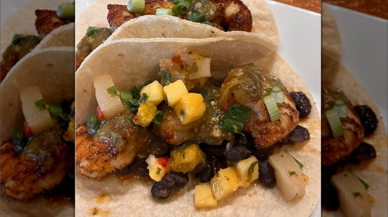 Two shrimp tacos with black beans and mango salsa on corn tortillas