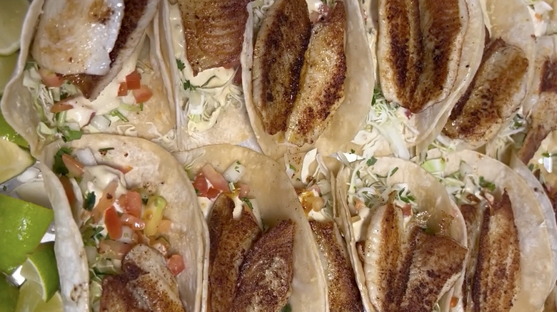 Top view of several fish tacos on corn tortillas with limes on the left