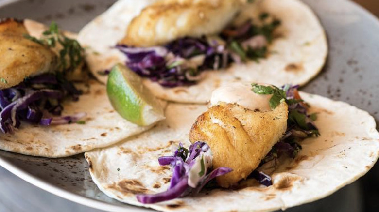 Three fish tacos on flour tortillas with slaw and lime