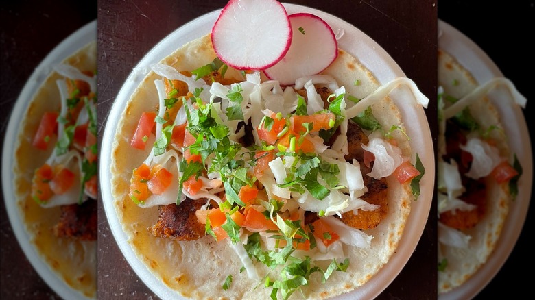 Salmon taco with slaw on a corn tortilla topped wit radish