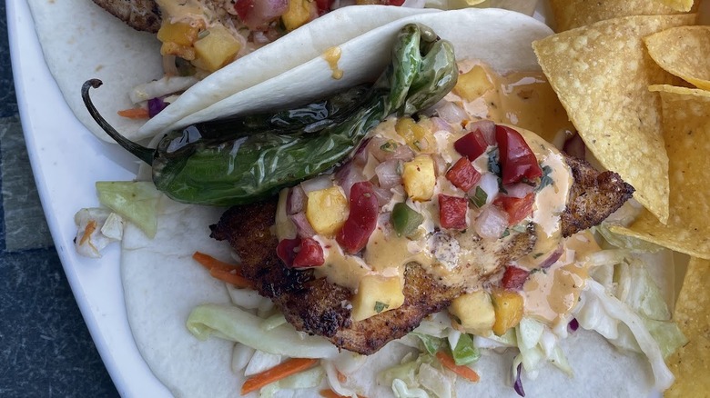 Fish taco with blistered pepper on flour tortilla with colorful garnishes and sauce