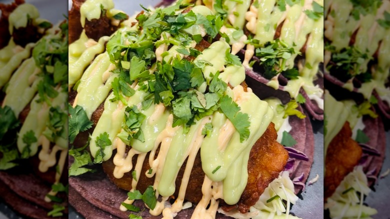 Close-up of fried fish taco with white and green sauce drizzled on top