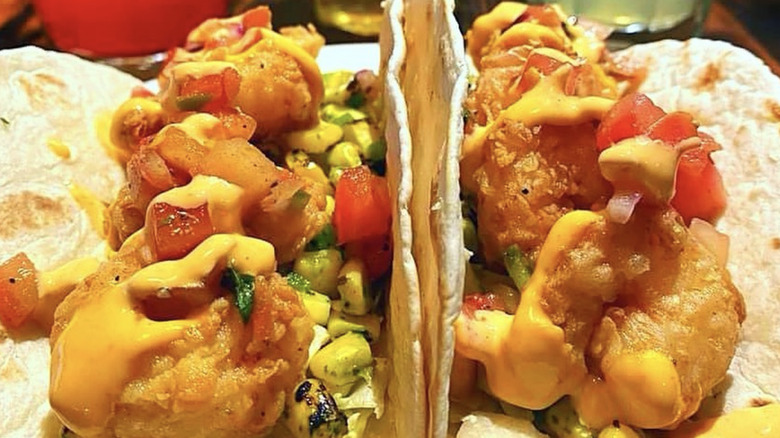 Two fried fish tacos with sauce on flour tortillas with garnishes and sauces