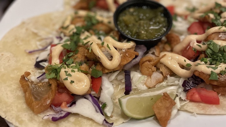 Salmon tacos on corn tortillas with salsa verde cup in the middle