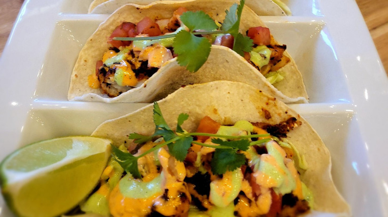 Two fish tacos on corn tortillas on a white tray