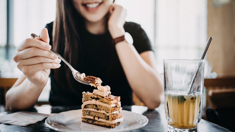 Smiling woman eating cake alongside iced beverage