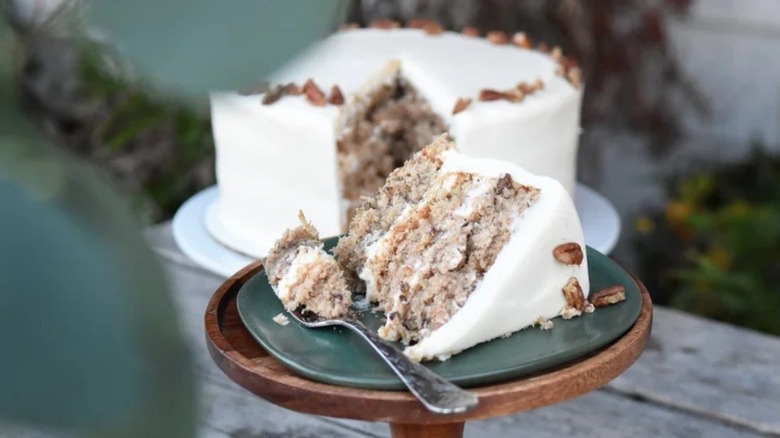 Slice of hummingbird cake on stand with whole cake in background