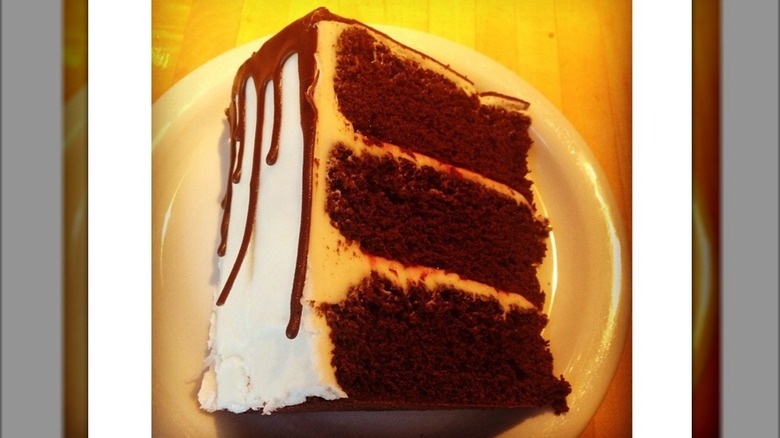 Slice of three tiered cake on plate with chocolate ganache