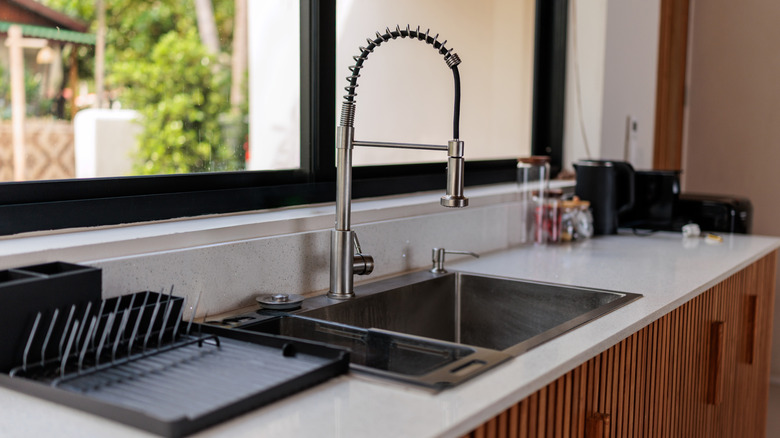 Large kitchen sink set into a white stone countertop with large windows behind it