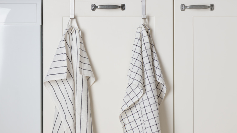 One striped and one blocked kitchen towels hanging from over-the-door hooks