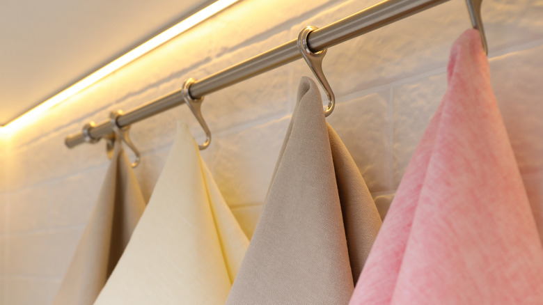 A towel bar with hooks holding several kitchen towels