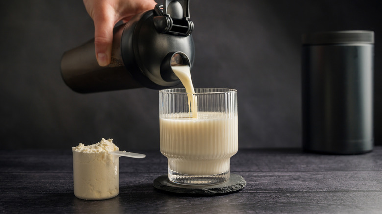 A scoop of protein powder next to a drink being poured from a shaker into a glass.