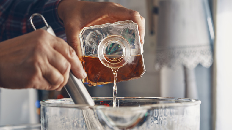 person pouring liquor into dish with ingredients for cooking