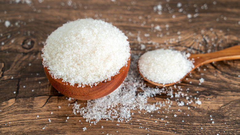 Spoon and bowl full of sugar on a wooden table
