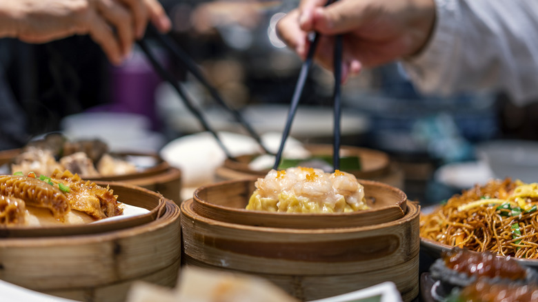 Various Chinese food dishes, some in bamboo steamers with people helping themselves with chopsticks