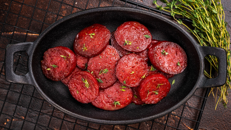 Sliced roasted beets arranged in black cast iron baking dish next to bundle of fresh thyme