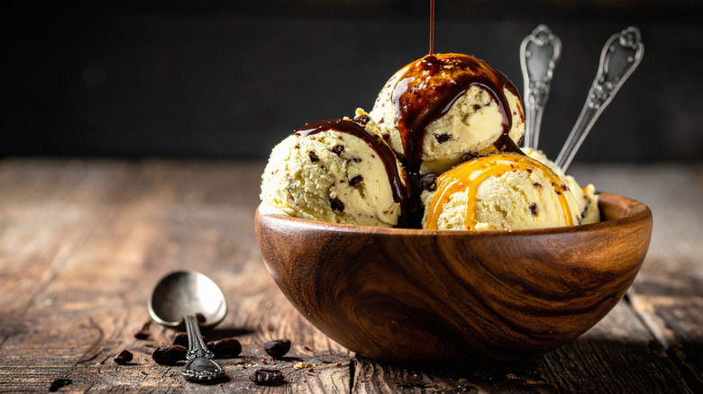 Three scoops of chocolate chip ice cream in wooden bowl with chocolate and caramel syrup.