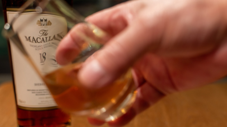 Glass of whisky being held in front of a Macallan bottle