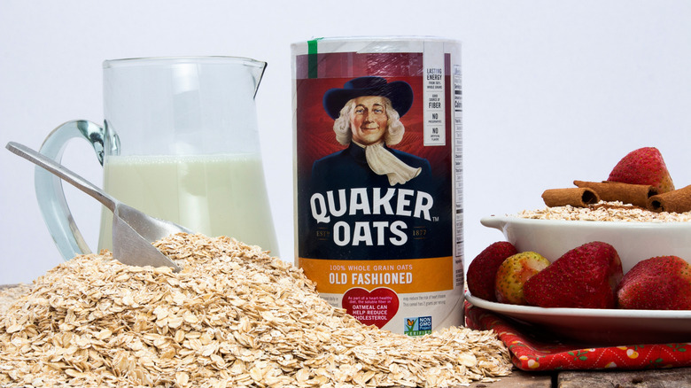 Canister of Quaker Oats next to milk jug, pile of oats, and bowl of oats with fruit and cinnamon
