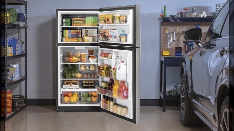 A GE garage-ready top freezer refrigerator installed in a home garage next to an automobile and shelving