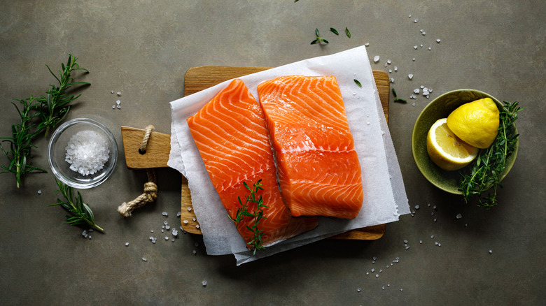 Fresh, raw salmon filets on a cutting board with lemon and salt in bowls nearby.