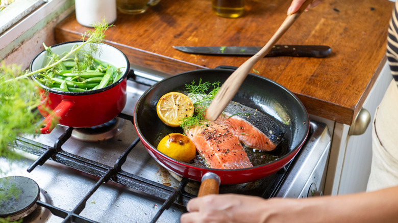 A person pan frying salmon on a stove.
