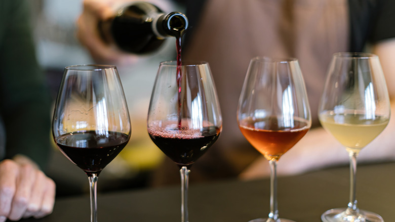 Four wine glasses arranged for a tasting as wine is poured into one