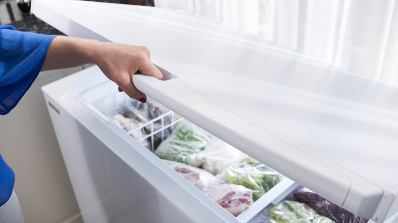 Hand opening a chest freezer filled with food