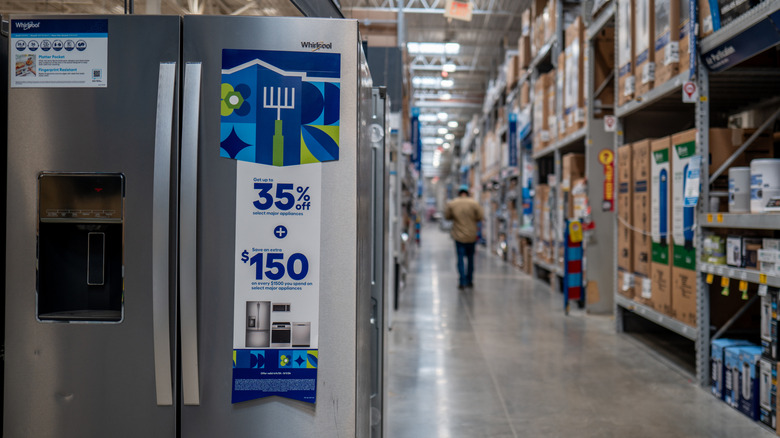 A Whirlpool refrigerator on display at Lowe's, with a customer walking down the aisle in the distance