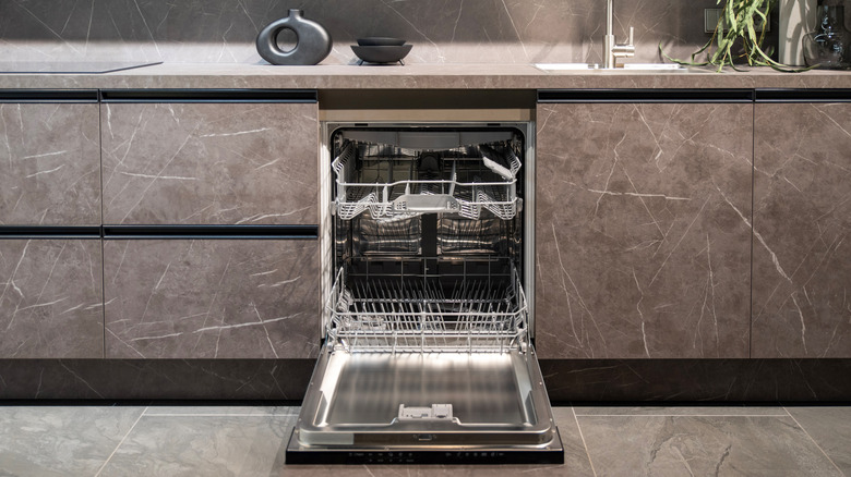 A dishwasher sits open in a marble kitchen