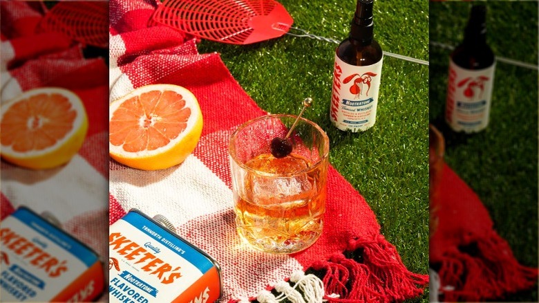 A bottle of Skeeter's Nootkatone Flavored Whiskey next to an old fashioned at a picnic.