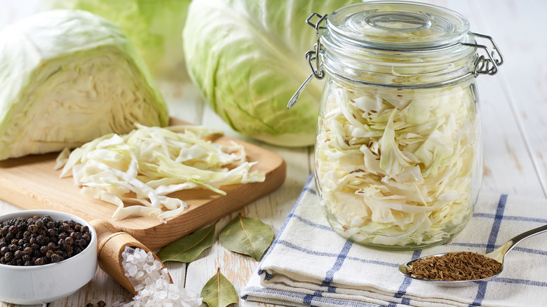 Chopped green cabbage and jar full of chopped cabbage with spices on the table as part of a process of making sauerkraut.