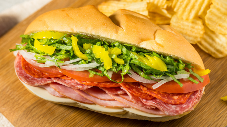 A classic Italian sub on a wooden surface next to potato chips