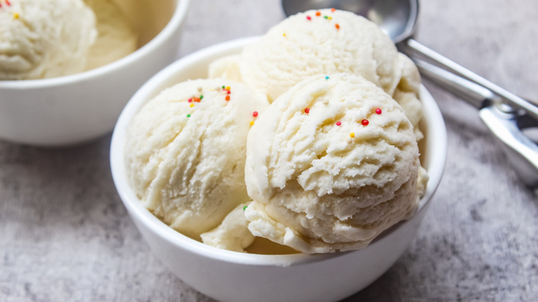Three scoops of vanilla ice cream with a few sprinkles, in a white bowl.
