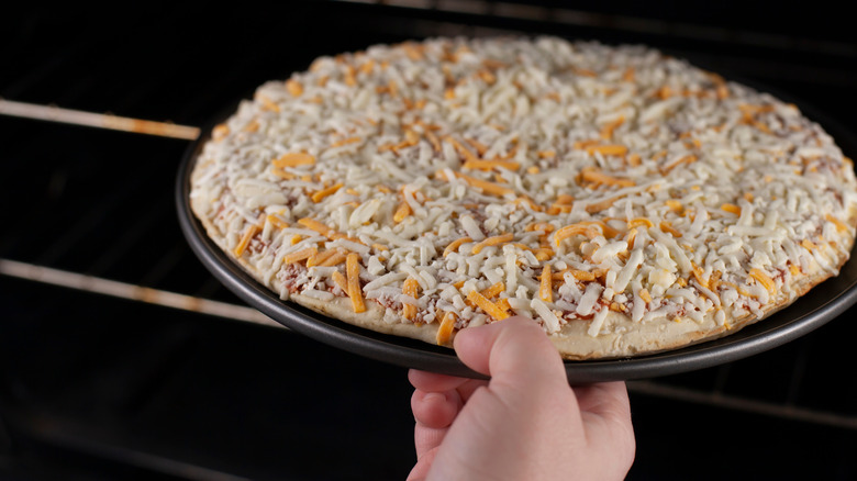 hand placing frozen pizza into oven