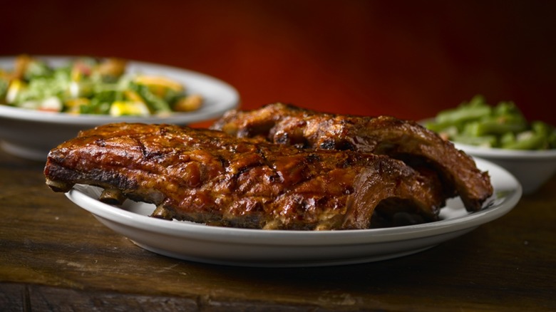 A plate of Texas Roadhouse ribs sitting on a wooden table, A bowl of green beans and one of salad sit in the background