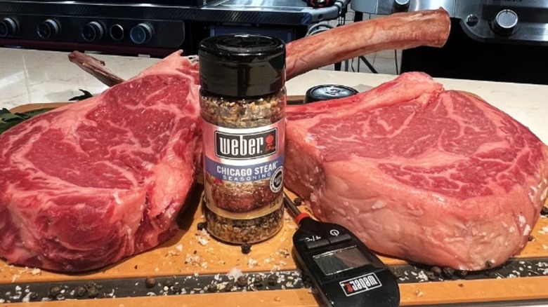 Two tomahawk steaks beside a bottle of Weber Grill seasoning and a Weber Grill thermometer