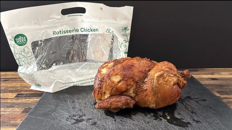 a rotisserie chicken on a cutting board next to a whole foods bag