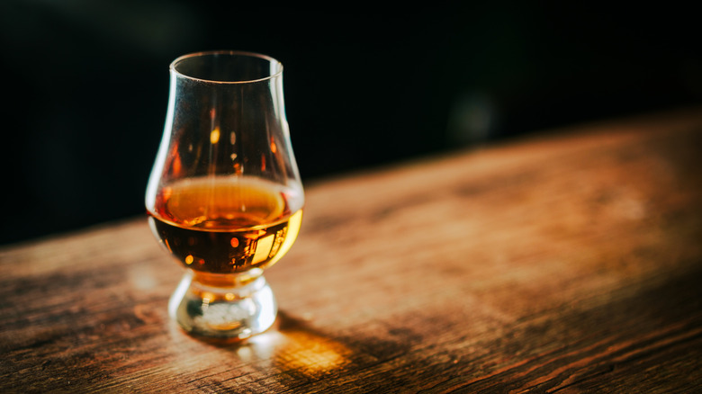 A dram of whisky in a glencairn glass on a wooden surface against a dark background.