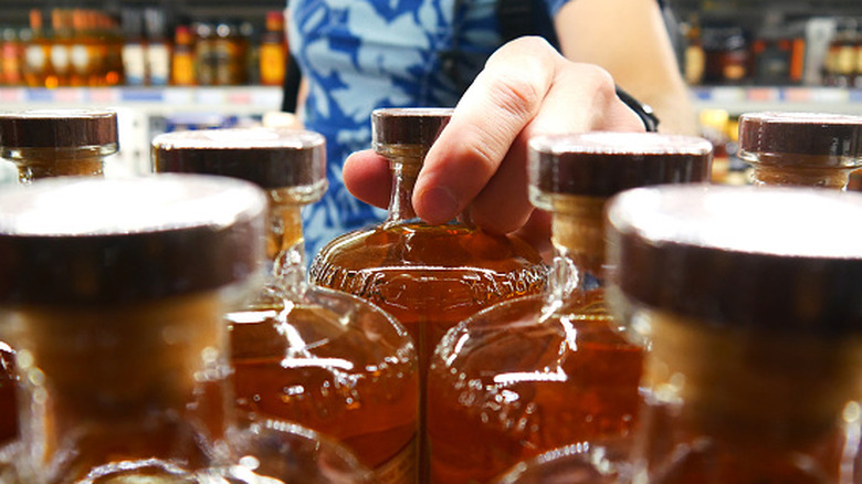 Person selecting bottle of whiskey from liquor store shelf.