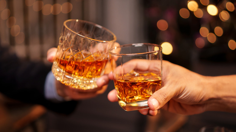 Two hands toasting glasses of whiskey.