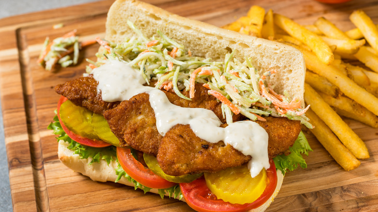 Sandwich with tartar sauce next to pile of fries on wooden board