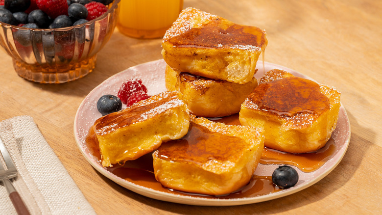 A plate of King's Hawaiian rolls French toast with fresh berries, powdered sugar, and maple syrup
