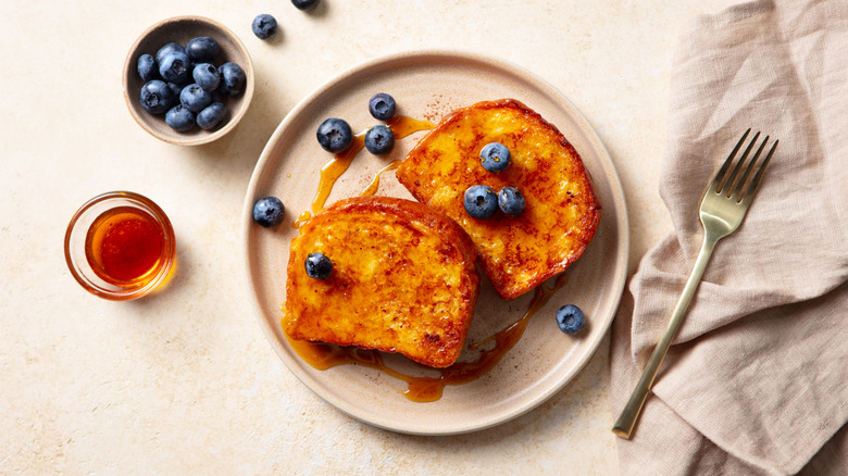 A plate of french toast topped with maple syrup and blueberries