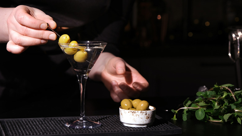 Bartender garnishing martini with skewer of olives