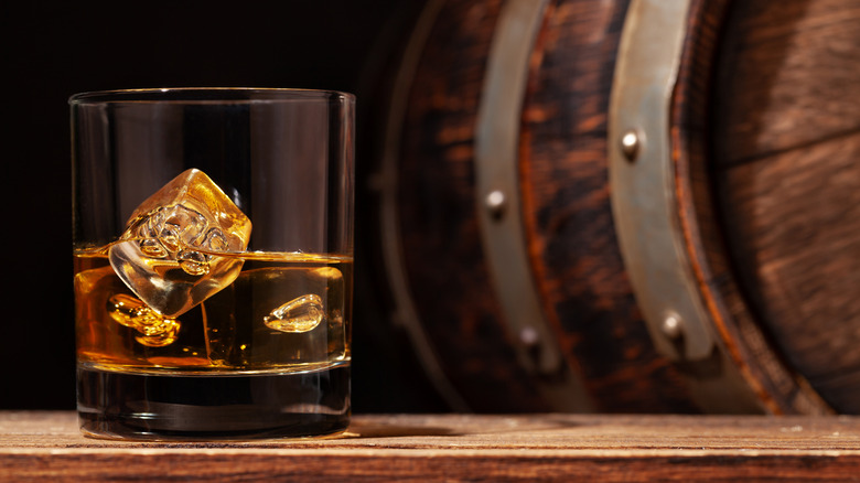 A glass of whisky in front of a whisky barrel 