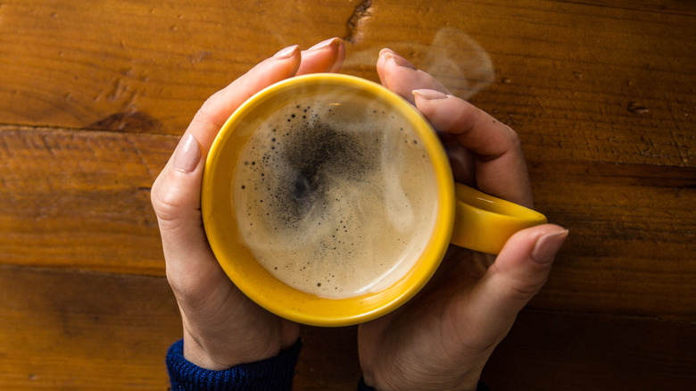 overhead view of hands holding yellow cup of black coffee