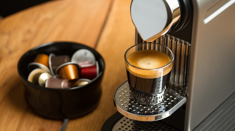 Nespresso coffee machine with a glass and pods in the background